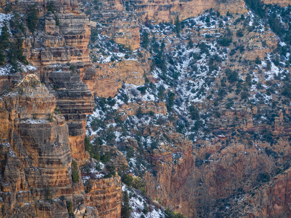 Steep rocky cliffs, with white snow and small green shrubs anywhere it levels off enough to collect soil.